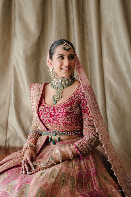 Stunning pink and red bridal lehenga with a heavy full sleeved blouse and emerald jewellery 