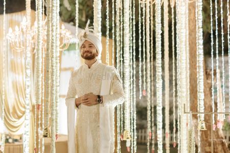 groom in traditional cream sherwani with gold embroidery against floral decoration 