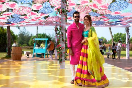 A color-coordinated couple in bright outfits for their day mehndi ceremony