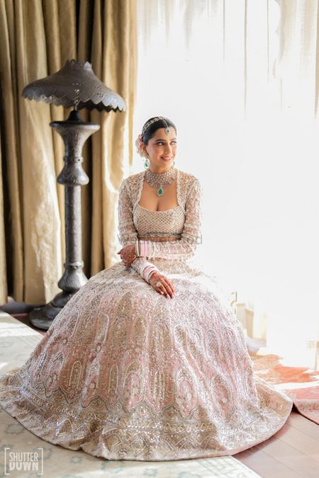 Beautiful bridal portrait with the bride in a full sleeved square neck blouse and a white and pink lehenga and light pink chooda