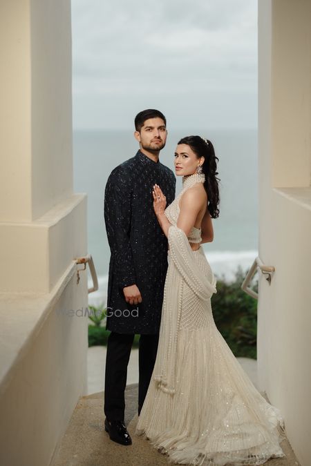 Photo of Lovely couple portrait with the groom in a navy blue sherwani and bride in an all white lehenga with pearl detailing.
