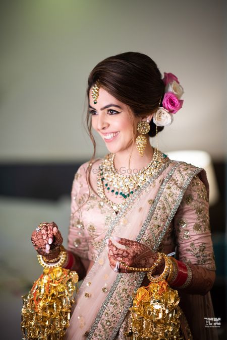 A bride in a blush pink lehenga and gold jewelry smiling for the camera