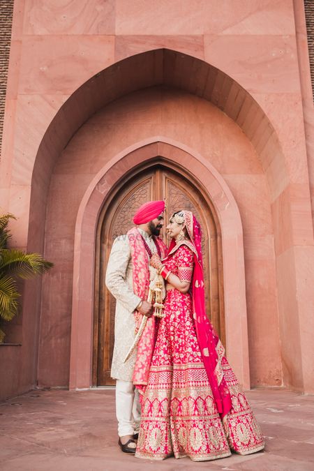 A sikh bride and groom in coordinated outfits pose on their wedding day