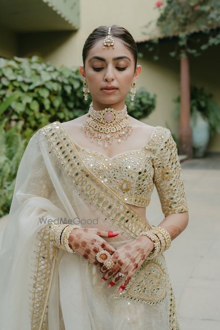 White and gold lehenga with mirror work and bride in layered bridal jewellery