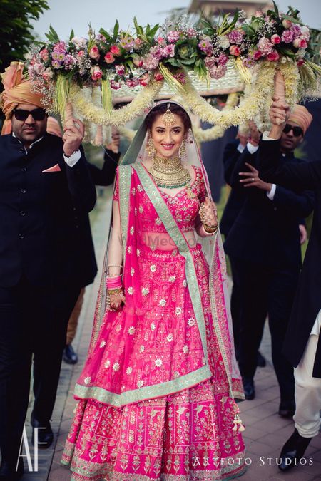Bride in bright pink entering under pretty phoolon ki chadar 