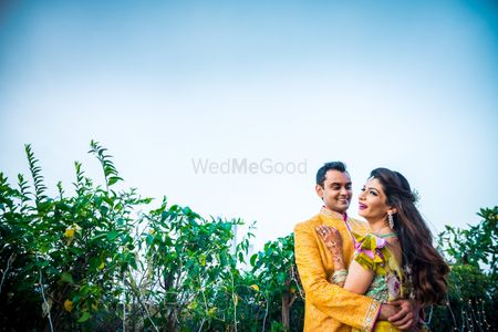 A bride and groom to be in yellow pose at their mehendi ceremony
