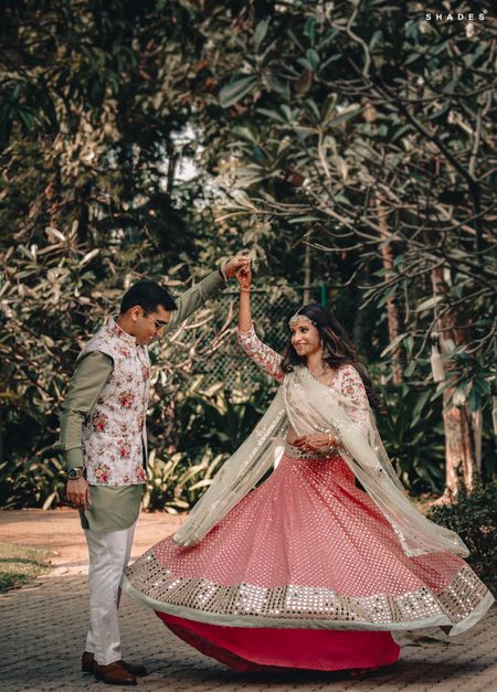 A bride in a sequinned pink lehenga twirling with her husband 