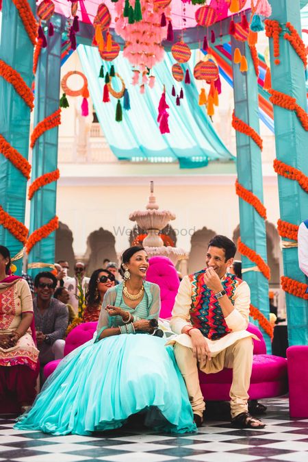 A couple sits under a colorful tent setup for the mehndi