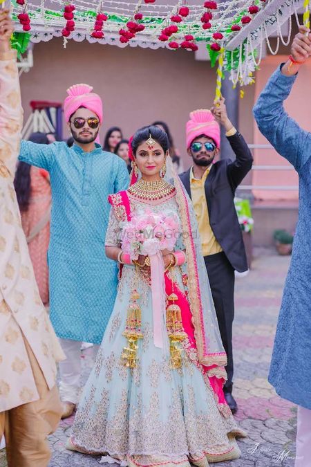 A bride in powder blue lehenga enters with a bouquet in hand.