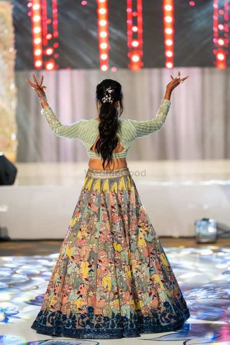 Photo of dancing bride wearing sage green floral embroidered lehenga and ponytail
