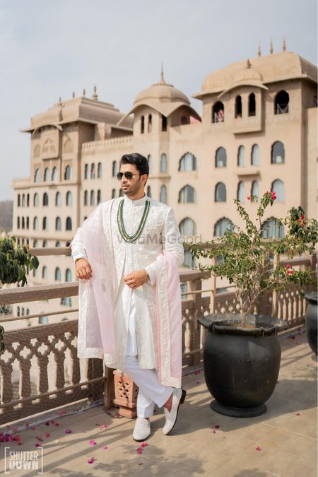 Photo of Wedding day groom portrait in a white and light pink sherwani