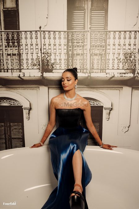 Stunning shot of the bride posing in a bathtub in a strapless cocktail gown with a sleeked back bun hairstyle