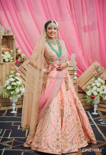 Bride in bright peach lehenga with green necklace 