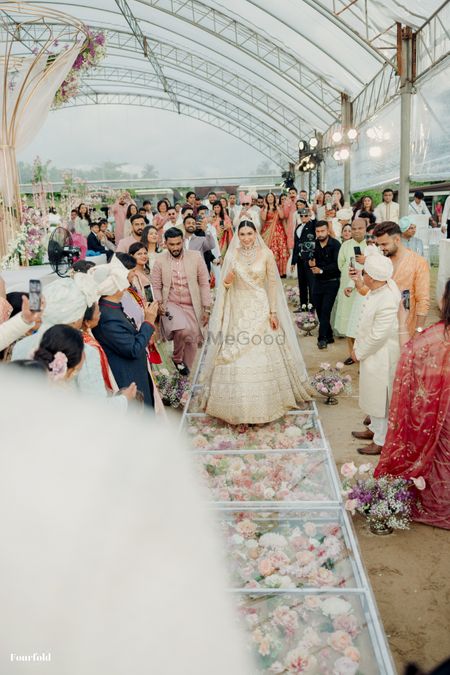 Bride walking down the aisle on floral box aisle in a gorgeous all white lehenga