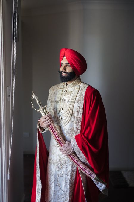 A groom dressed in a white sherwani with red turban and red shawl