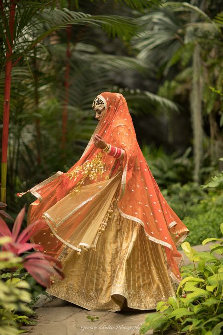 Photo of Gold lehenga with orange dupatta twirling bride