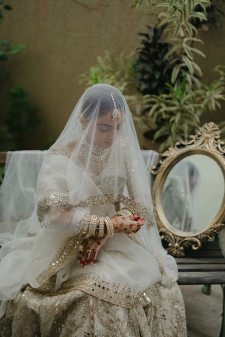Bridal portrait with the bride holding a sheer veil with a white and gold lehenga