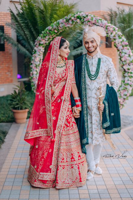 Photo of groom sherwani in white and green with bride in red