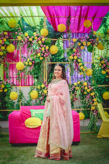 Photo of A bride to be poses in front of her pop of color mehendi decor