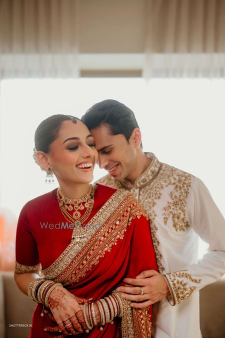 A lovely candid portrait of the couple on the wedidng day with the bride in a red saree and layered gold jewellery with the groom in a white and gold sherwani kurta