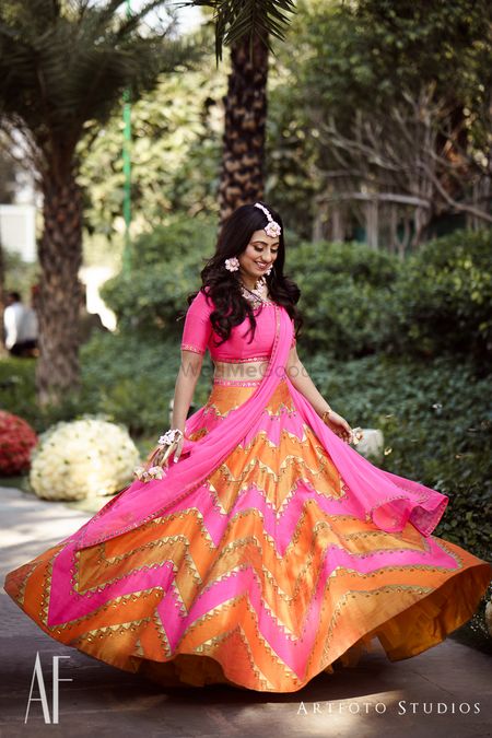 Bride twirling in bright pink and orange mehendi lehenga 