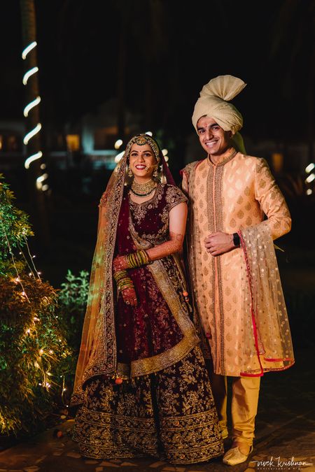 Photo of Contrasting bride and groom with maroon lehenga and peach sherwani