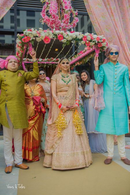 Bride in peach entering under pink phoolon ka chadar 
