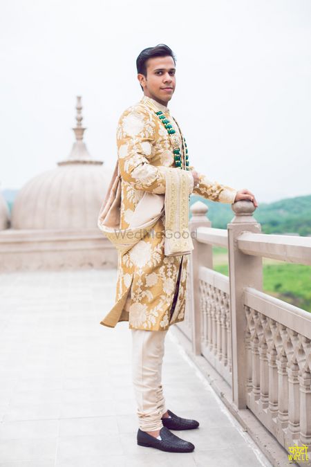 Groom in gold and white sherwani with green necklace