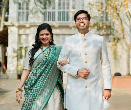 Matching bride and groom in white with bride holding green banarasi dupatta