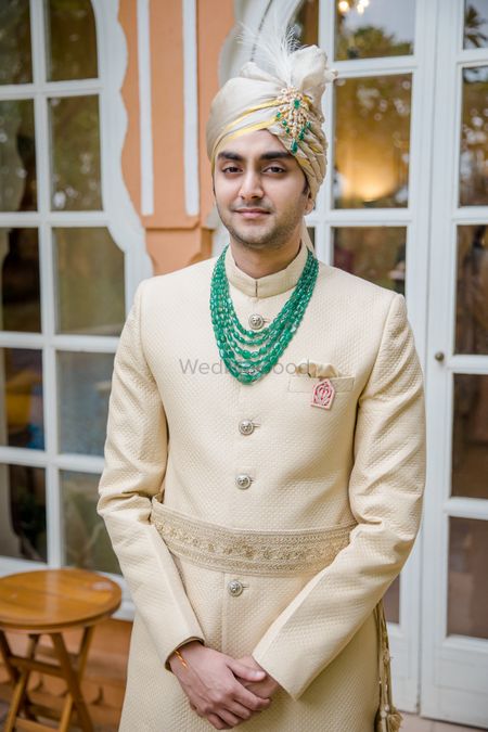 Groom wearing an off-white sherwani with a layered necklace.