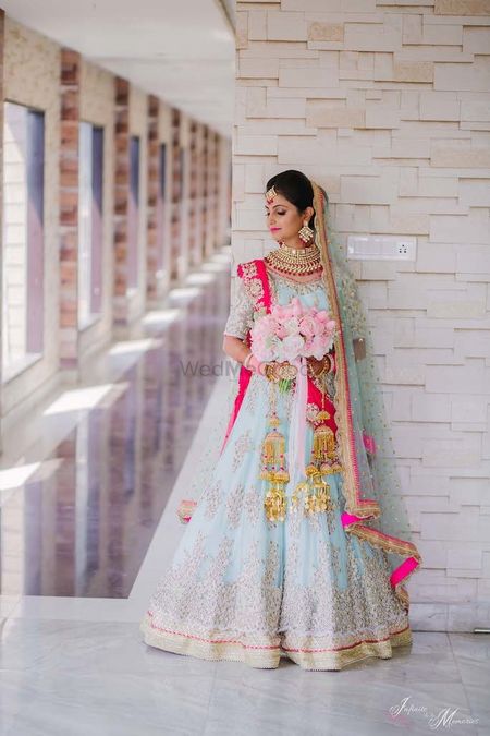 A bride in powder blue lehenga holding a bouquet of roses
