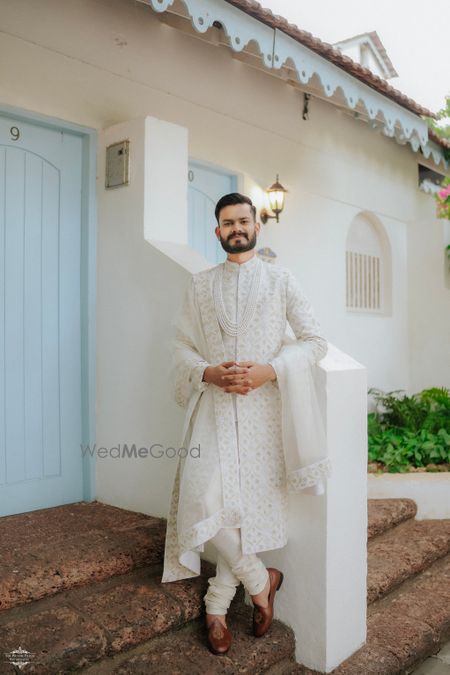 Photo of A monotone all-white sherwani with matching pearls and contrast juttis for the groom on the wedding day
