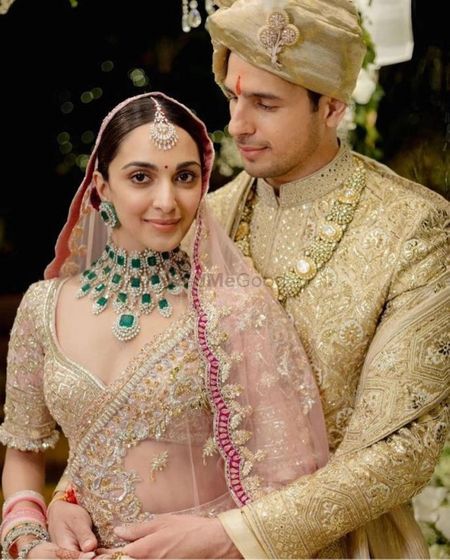 Photo of kiara advani wearing light pink lehenga and contrasting emerald jewellery on her wedding day