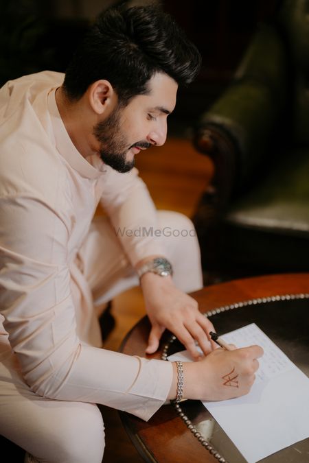 A groom to be writing his vows and a love letter to the bride to be in a peach sherwani