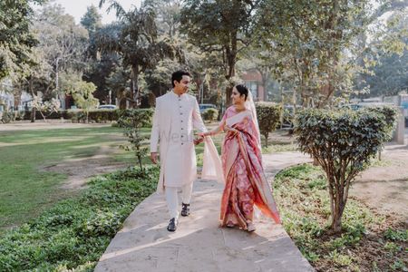 Photo of groom in cream sherwani and bride in silk saree walking at the park