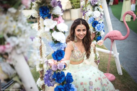 bride on mehendi with floral swing and white lehenga