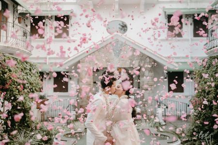 Romantic shot of the couple kissing and being showered with light pink rose petals