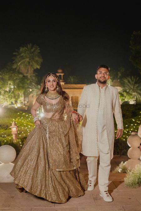 Lovely couple entry shot with bride in a shimmery gold lehenga and groom in an ivory sherwani