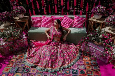 Bride in her bright pink lehenga posing in front of her beautiful Mehendi seating. 