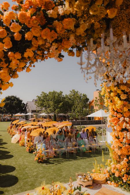 Stunning burnt orange floral decor for an outdoor mandap with matching parasol umbrellas for the guests