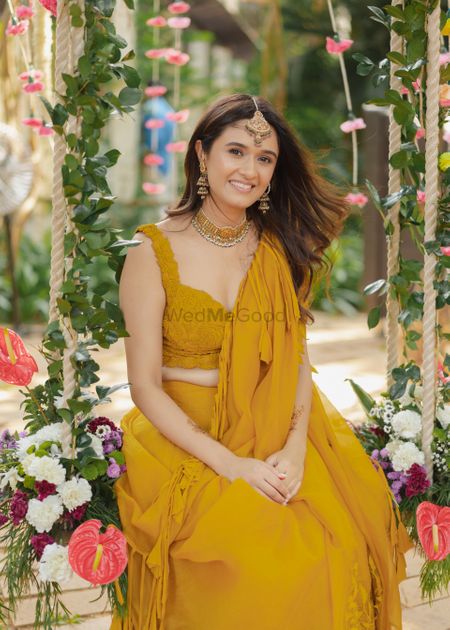 Lovely bride wearing an ochre yellow ruffled lehenga set and sitting on a floral swing