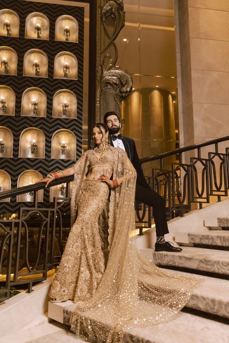 Classy couple portrait with the bride in a gold lehenga co-ord set with cape dupatta and the groom in a black tuxedo