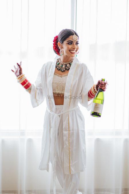 Photo of bride wearing a robe holding a champagne getting ready shot