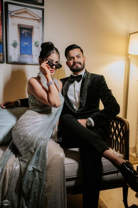 Photo of Dramatic couple shot with the bride in a silver saree and halter neck blouse with sunglasses and groom in a black tux