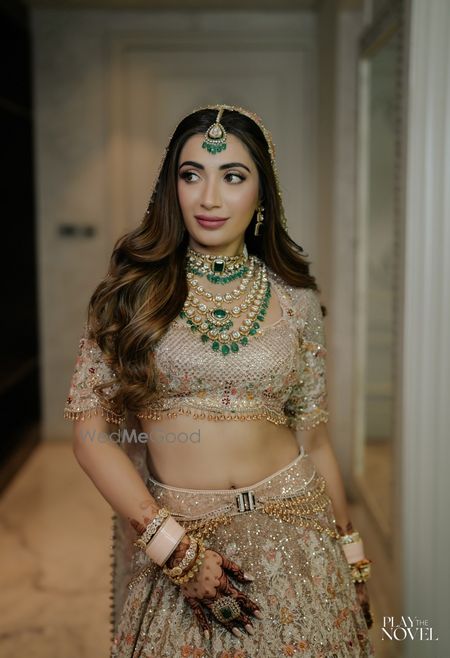Photo of Stunning bridal portrait in a gold lehenga, layered emerald jewellery and a unique open hairstyle on her wedding day