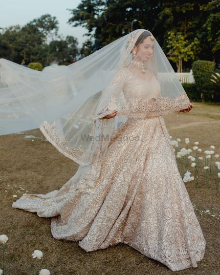 Photo of Gorgeous bridal entry in a gold and white lehenga with a veil and train.
