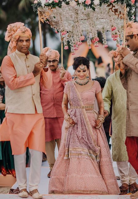 A bride in pink entering under a phoolon ki chaadar with her brothers