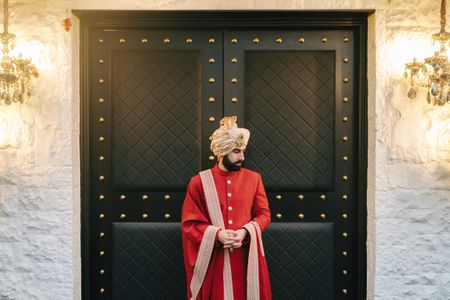 Classic groom portrait with groom in an all-red sherwani with gold details and a matching gold pagdi