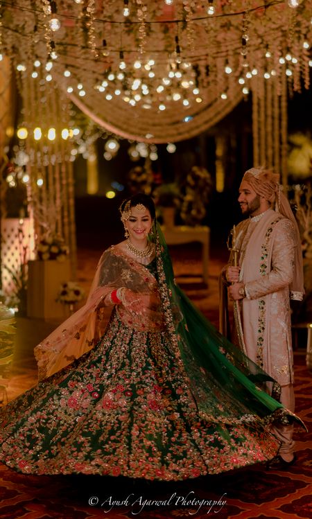 A bride in green lehenga twirling while the groom looks on 