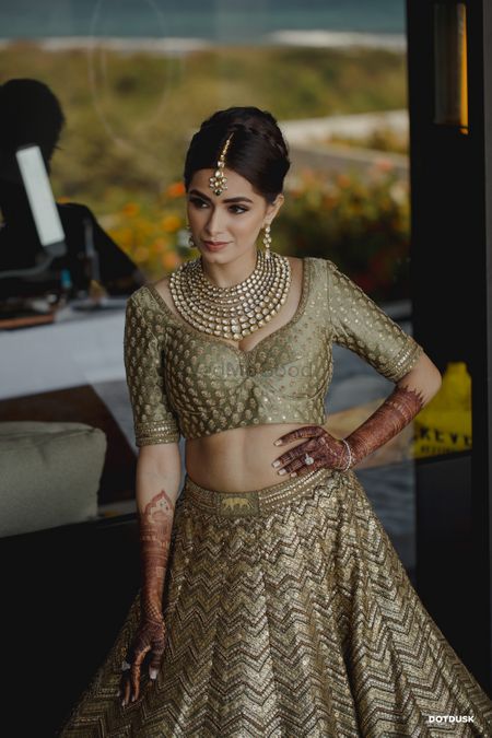 Photo of A bride posing while getting ready wearing an olive gold Sabyasachi lehenga
